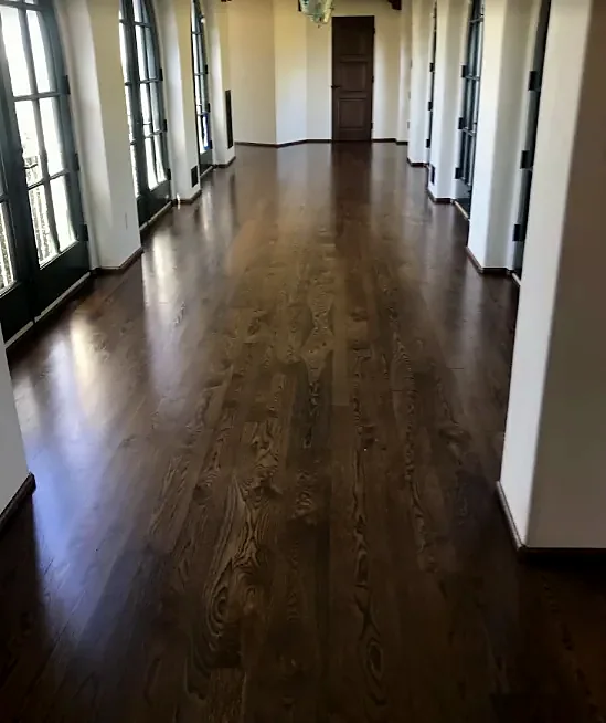 A long gallery with a dark stained oak floor, arched glass doors on both sides and a wood door at the end