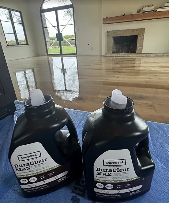 Two jugs labeled DuraSeal DuraClear Max water-based finish on a blue tarp, with a glossy finished floor behind them