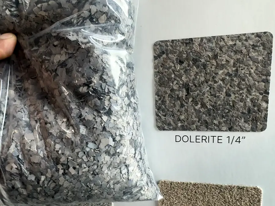 Una bolsa de hojuelas grises junto a una muestra de hojuelas con la etiqueta Dolerite 1/4 de pulgada