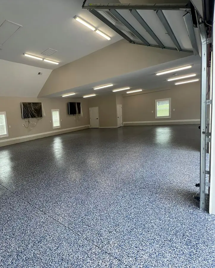 Garaje amplio con piso epóxico de hojuelas azules y grises, luces en el techo y la puerta levantada