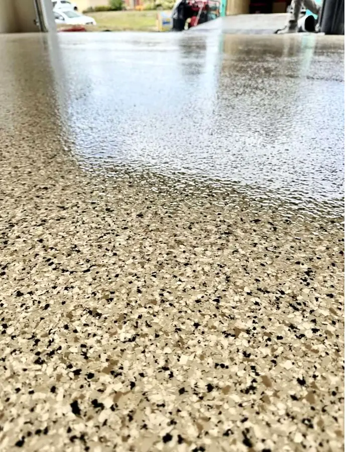Vista cercana de un piso epóxico de hojuelas beige, negras y blancas con acabado brillante