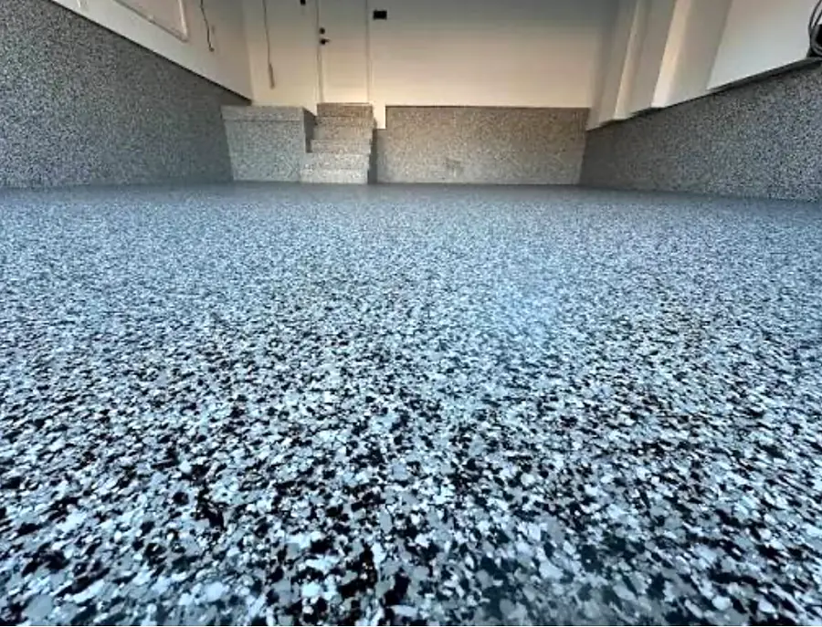 Vista amplia de un piso de garaje con hojuelas grises, negras y blancas, y el mismo acabado subiendo por la base de las paredes