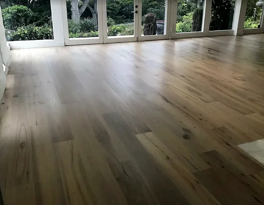 A long room of mixed-tone wide planks with a full wall of glass doors on a garden