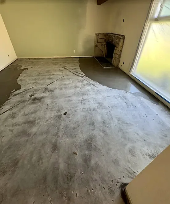 Gray leveling compound poured partway across a room with a stone fireplace