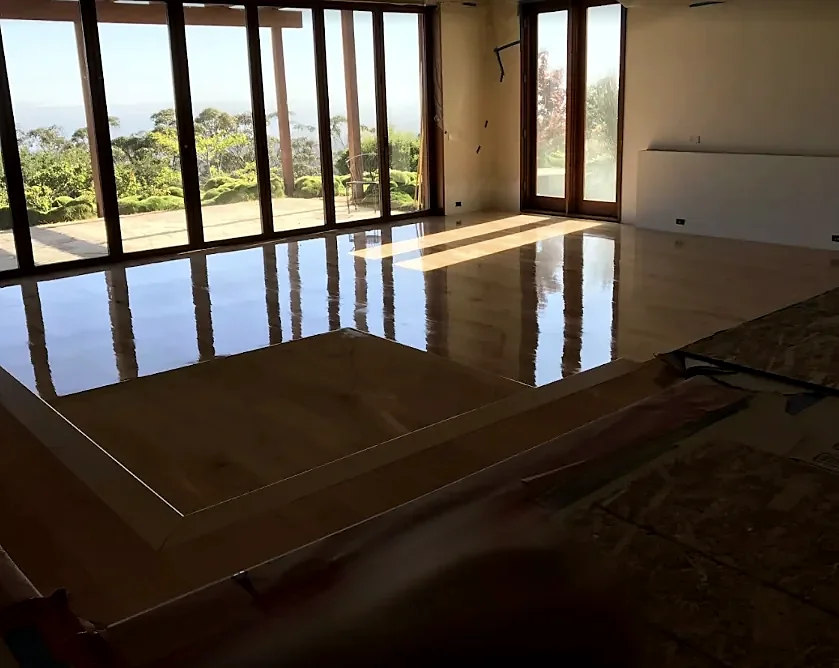 A freshly coated floor mirrors a wall of glass doors that look out over a garden to the ocean