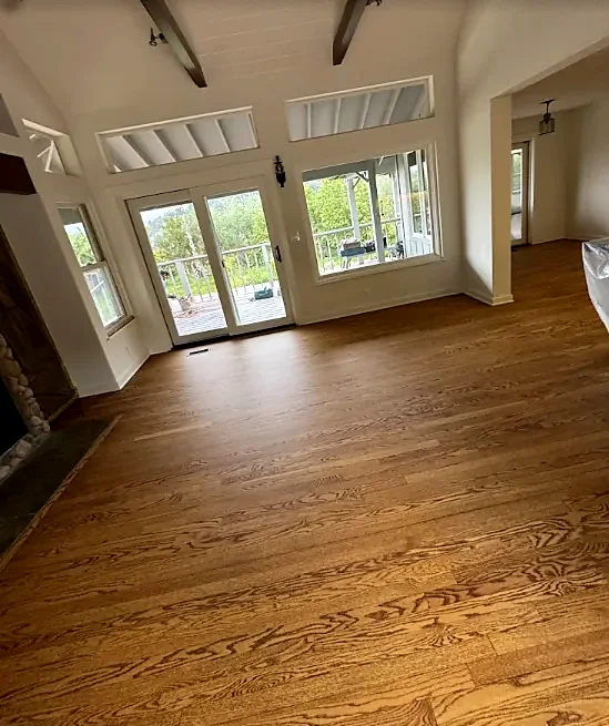 A room with a warm brown strip oak floor, a beamed ceiling and windows on a garden