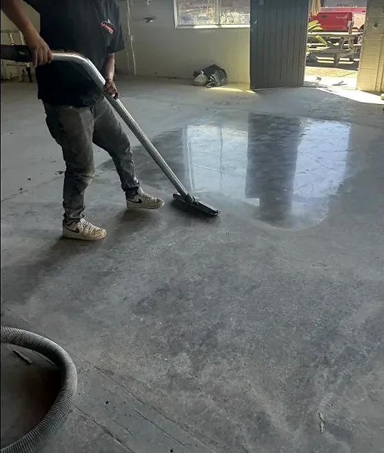 A crew member vacuums a concrete floor in a commercial space, part of it already shining