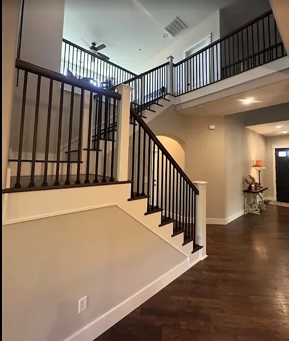 A two-story entry with a dark wood floor, dark stair treads and black iron balusters