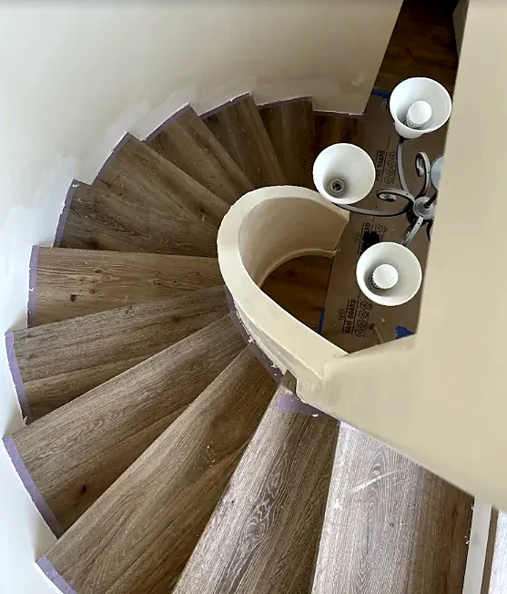 A curved stair seen from above, each wedge-shaped tread covered in gray-brown wood