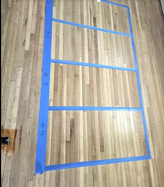 Five sample boxes marked in blue tape on a sanded oak floor, each numbered