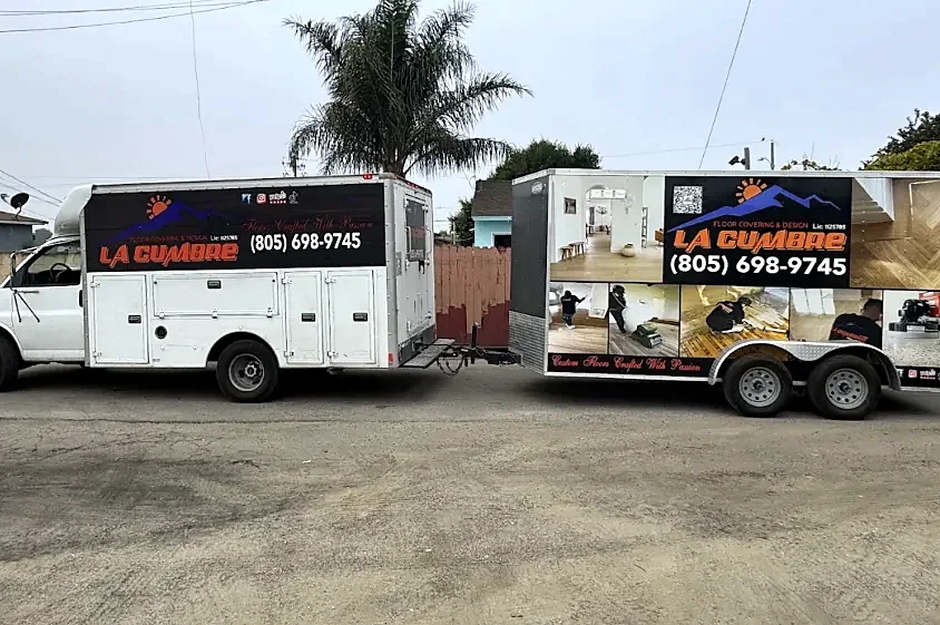 A white La Cumbre work truck towing an enclosed trailer wrapped with job photos and the phone number