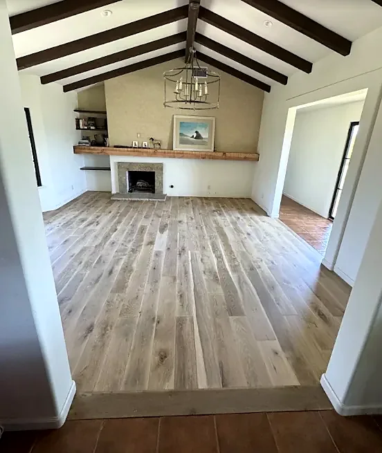 A vaulted room with dark beams and a fireplace, seen from a step down onto a light plank floor