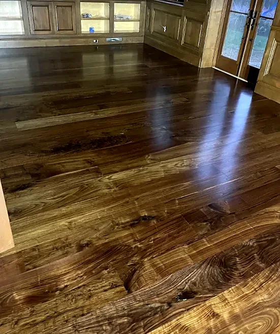 A wide plank floor with strong dark grain and a satin shine, in a room with wood-paneled cabinets and glass doors